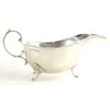 A George V silver sauce boat, with a shaped edge, scroll handle and shaped legs, headed by leaf