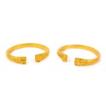 A pair of open bracelets, cast with stylised ends, unhallmarked yellow metal.