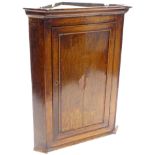 An early 19thC oak and mahogany cross banded corner cabinet, with a moulded inverted breakfront