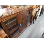 A mahogany bookcase with two glazed doors, flanking a central flat panel door on bracket feet.