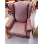 A brown leatherette wingback armchair on turned tapering legs.