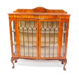 An early 20thC serpentine walnut display cabinet, with a pair of glazed doors opening to reveal