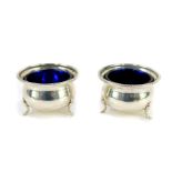 A pair of George V silver circular salts, with blue glass liners raised on three paw feet,
