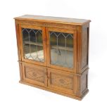 An Inglesants oak cupboard bookcase, with two glazed doors opening to reveal a single shelf, over