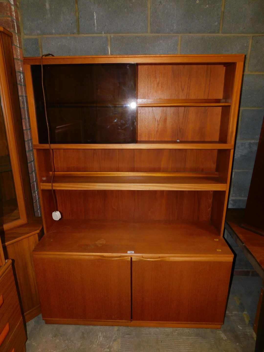 A late 20thC teak lounge unit, the top with glazed doors and shelves over a sideboard base, 171cm