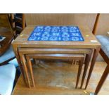 A mid 20thC teak nest of tables, inset with blue and white floral tiles, no makers label, largest