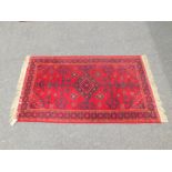 A Kalif wool rug, red ground with central diamond motif and diamond border, 162cm x 91cm.