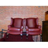 A pair of maroon leather wingback armchairs, raised on cabriole legs.