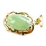 An oval brooch, with central pale green jadeite type stone, the scroll design frame with four claw