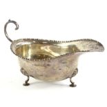 A George V silver sauce boat, with a beaded border, scroll handle, on shaped legs, London 1912,