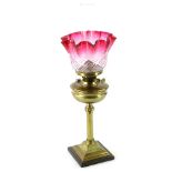 A Victorian brass oil lamp, with cranberry tinted moulded glass shade, the base with reeded column