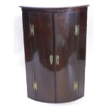 An early 19thC mahogany bow fronted corner cabinet, the top with a moulded edge, above two ebony
