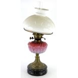A Victorian brass oil lamp, with white opaque shade, pink tinted reservoir, on a ceramic base,