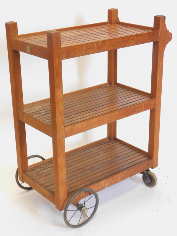 A teak slatted three tier trolley, on spoked wheels, label for Castles Ship Breaking Company