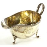 A George V silver sauce boat, with a gadrooned edge and scroll handle, on three shaped feet,
