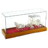 A continental white metal model of a carriage, pulled by two horses, in a glazed case, the case 38cm