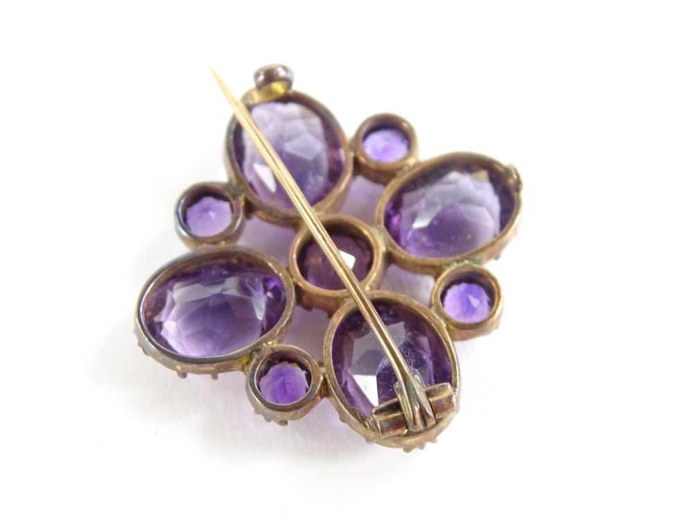 An amethyst set decorative brooch, with floral leaf design, flanked by two smaller stones, in a gold - Image 2 of 2