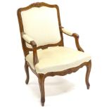 A French style walnut open armchair, upholstered in beige fabric to the back, arm rests and seat, on