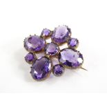 An amethyst set decorative brooch, with floral leaf design, flanked by two smaller stones, in a gold