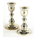A pair of white metal squat candlesticks, each with urn dish holders, inverted baluster stems and