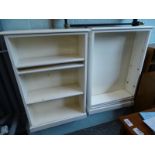 A pair of cream painted open book cases, each on a plinth base.