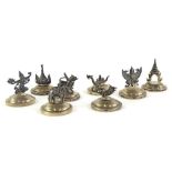 A set of eight white metal menu holders, each on domed circular bases, to include dragon, 3cm