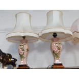 A pair of French pink ground pottery table lamps, painted with wild roses, with shades, 70cm high.