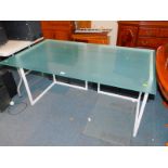 A modern glass topped table, raised on white metal L shaped supports, 73cm high, 140cm wide, 79.