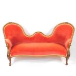 A Victorian walnut spoon back sofa, with serpentine seat, upholstered in red draylon, raised on