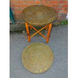 An Eastern brass top table, with folding wooden X frame base, together with another brass table top,