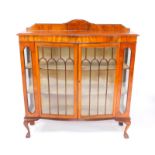 An early 20thC serpentine walnut display cabinet, with a pair of glazed doors opening to reveal
