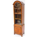 A mid 20thC walnut narrow display cabinet, the arched top raised above a glazed door, set with plain