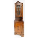 A mahogany finish freestanding corner cupboard, with shell cornice raised above a glazed door on