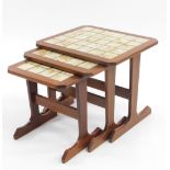 A nest of three vintage teak tables, each with tile tops and canted edges, on stiles terminating