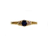 A 18ct gold dress ring, claw set with a central blue stone flanked by small diamonds, on a