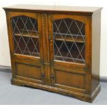 A late 20thC Old Charm style oak bookcase, with lead glass panel diamond shaped doors raised above a