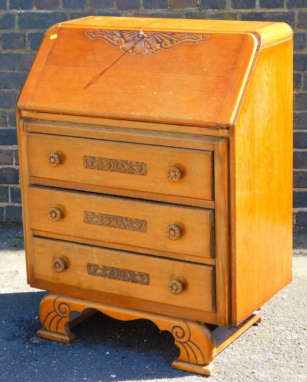 A mid 20thC oak bureau, with carved fall front, raised above three long drawers on shaped feet, 76cm