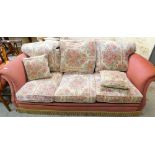 A three seater lounge settee, in floral cushions on pink ground, 206cm wide.