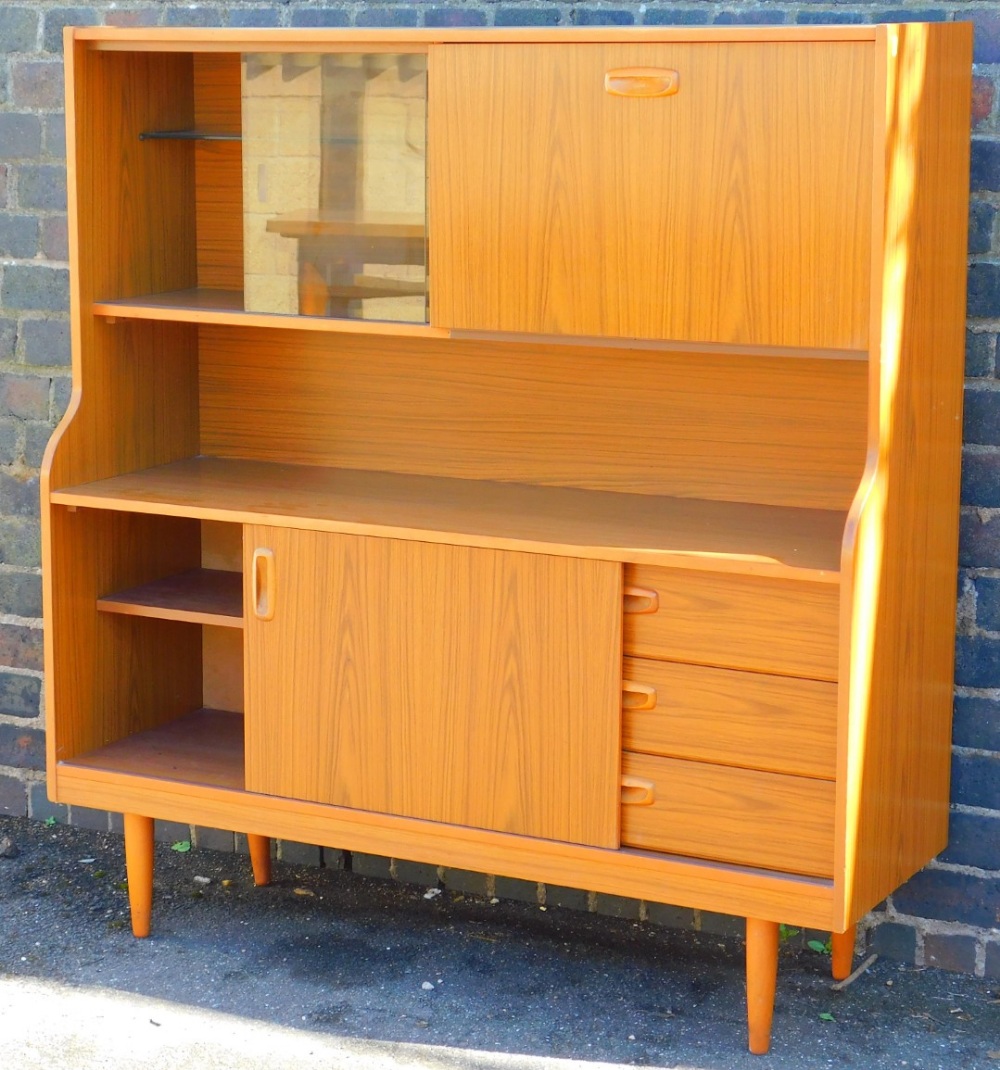 A teak cabinet with sliding glass doors raised above enclosed drawers on shaped legs, 123cm wide.