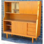 A teak cabinet with sliding glass doors raised above enclosed drawers on shaped legs, 123cm wide.