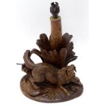 A late 19thC/early 20thC Black Forest Linden wood lamp base, carved with a hound beside some
