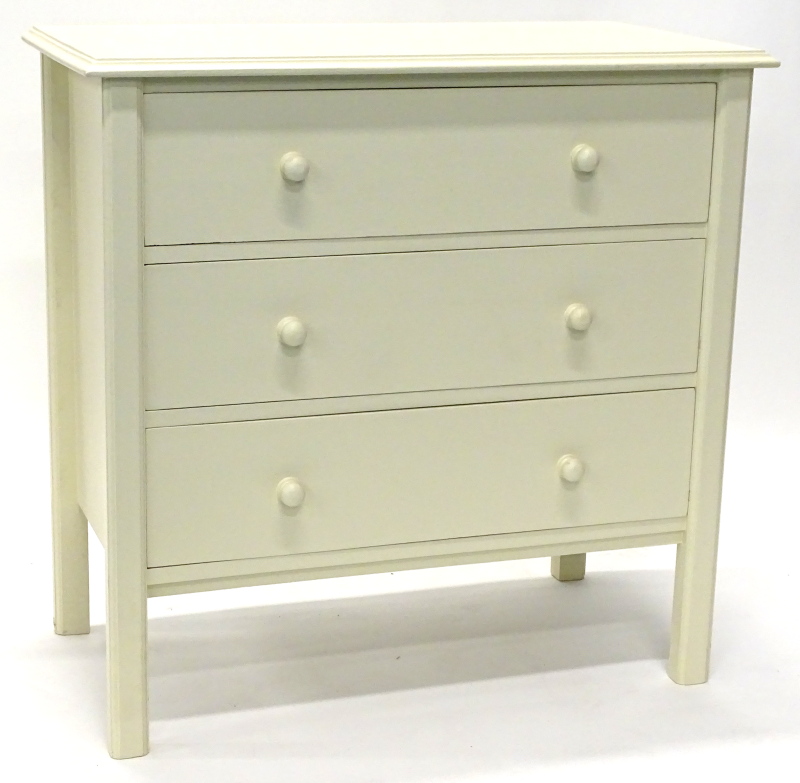 A cream painted chest of drawers, the top with a moulded edge above three legs, each above turned