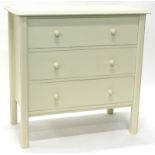 A cream painted chest of drawers, the top with a moulded edge above three legs, each above turned