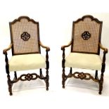 A pair of ebonised oak open armchairs, each with a caned back, shaped arms and a padded seat on