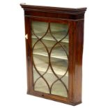 An early 19thC mahogany and boxwood strung glazed hanging corner cabinet, the top with a moulded