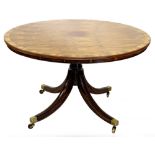 A circular rosewood tilt top table, with a turned column splayed legs and brass capped castors,