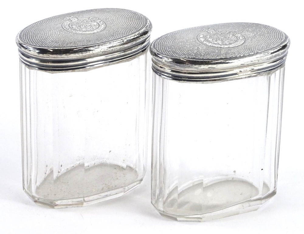 A pair of Victorian facetted oval cut glass dressing table jars, each with an engine turned lid with