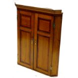 An early 19thC oak and mahogany cross banded hanging corner cabinet, with H shaped brass hinges,