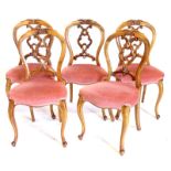 A set of five Victorian walnut balloon back chairs, each with a pierced splat, padded fabric seat on