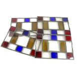 A set of four small rectangular stain glass panels, decorated in red, amber and blue, 24cm x 16cm.